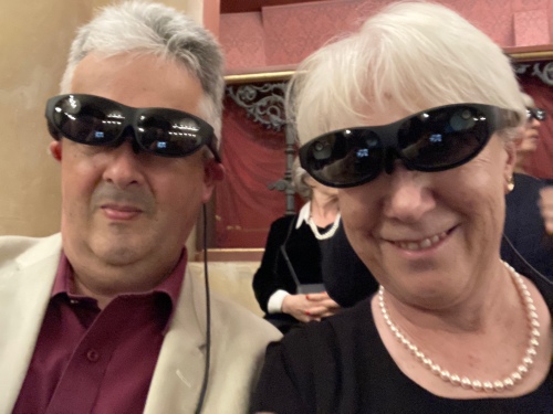 A man and a woman in smart clothes wearing ridiculous oversized black glasses. 