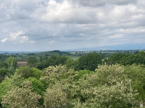 Landscape: trees in the near distance, then a large plain with a few small hills, and much higher hills beyond. 