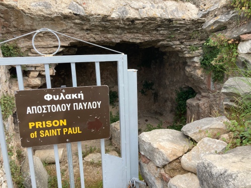 A metal gate, with a sign on it saying ‘Prison of St Paul’ in both Greek and English, barring the entrance to a nondescript room.